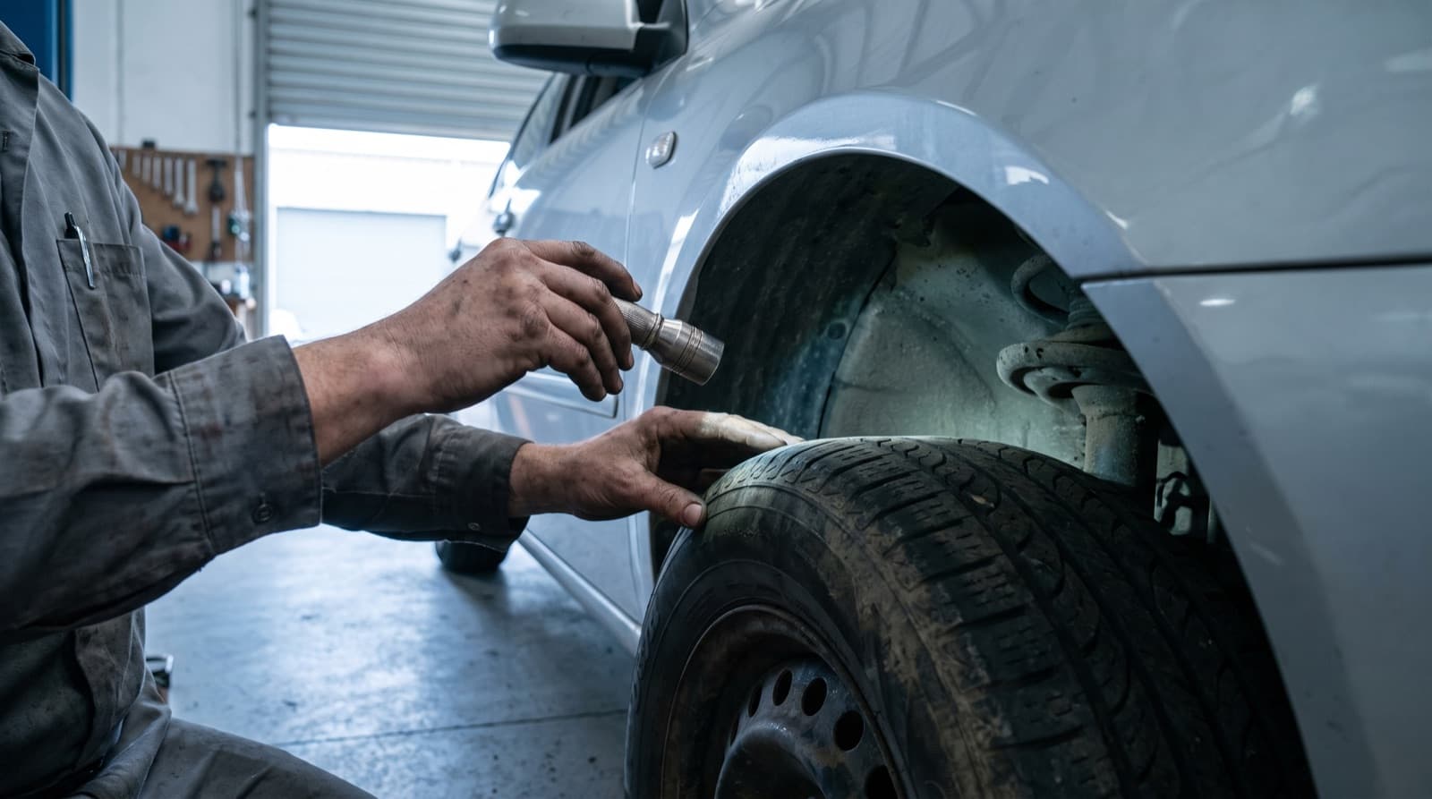 Manos de un técnico con una linterna revisando la llanta y el pase de rueda de un auto en un taller